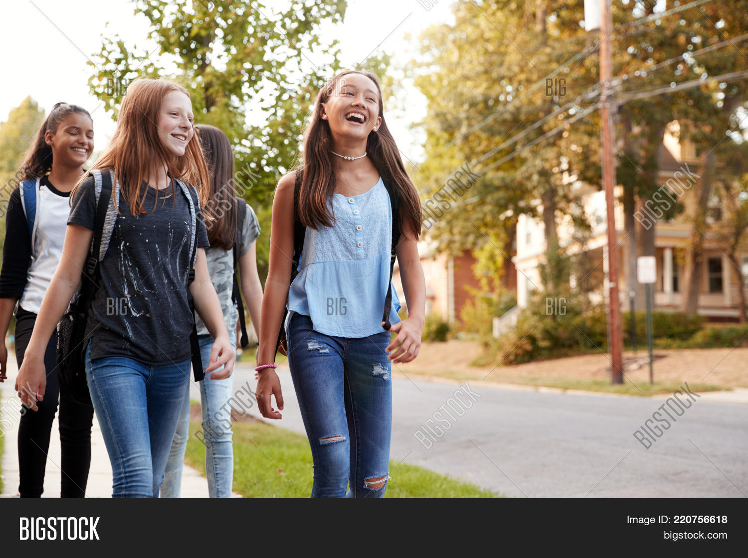 adolescence,backpack,bonding,carrying bag,casual clothing,caucasian,children,close up,communication,copy space,dark hair,day,four people,friends,friendship,front view,girls,girls only,grass,happy,hispanic ethnicity,horizontal,independent,jeans,journey,kids,laughing,long hair,looking away,low angle,multi-ethnic group,neighbourhood,outdoors,pavement,pre-teens,red hair,residential area,rucksack,selective focus,smiling,street,sunlight,talking,teenagers,three quarter length,togetherness,trees,walking to school,youth