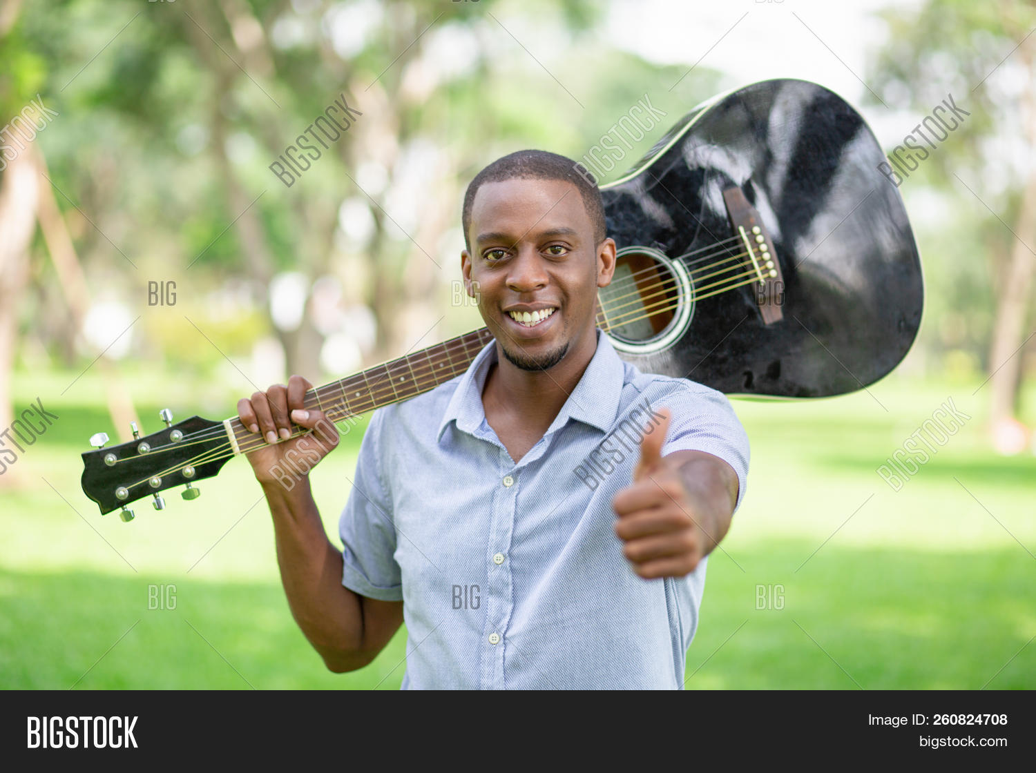 African,American,acoustic,adult,attractive,black,camera,casual,city,concept,fretboard,front,fun,grass,green,guitar,guitarist,guy,handsome,happy,holding,horizontal,instrument,leisure,lifestyle,looking,male,man,music,musical,one,outdoor,park,person,player,portrait,positive,rest,shirt,shoulder,showing,smiling,standing,student,success,summer,thumb,tree,up,young