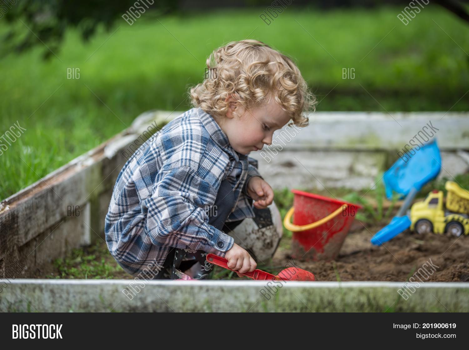 Young Caucasianboy With Curly Hair Playing In Sandbox