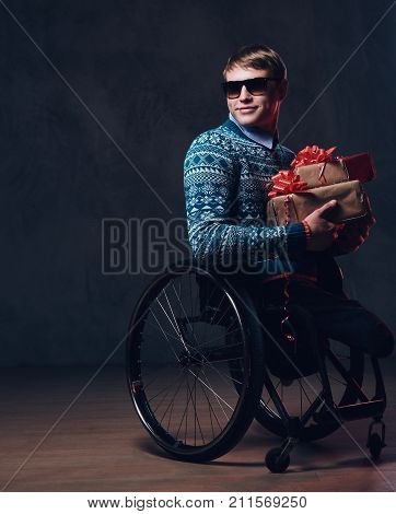 Positive man in wheelchair with Christmas gifts over dark grey background.