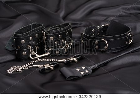 Leather Handcuffs, Nipple Clamps, Chain Collar And Stack On Black Silk Background. Accessories For A