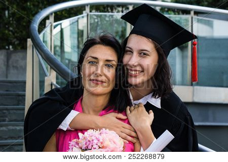 Young Beautiful Woman Graduate Hugging Her Mother At Graduation Ceremony, University Graduation Cert