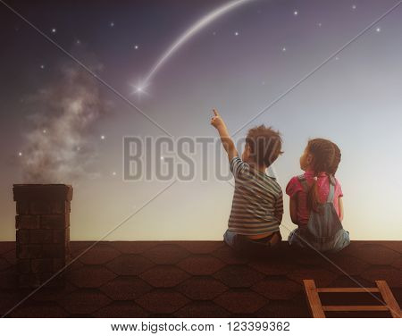 Two cute children sit on the roof and look at the stars. Boy and girl ...