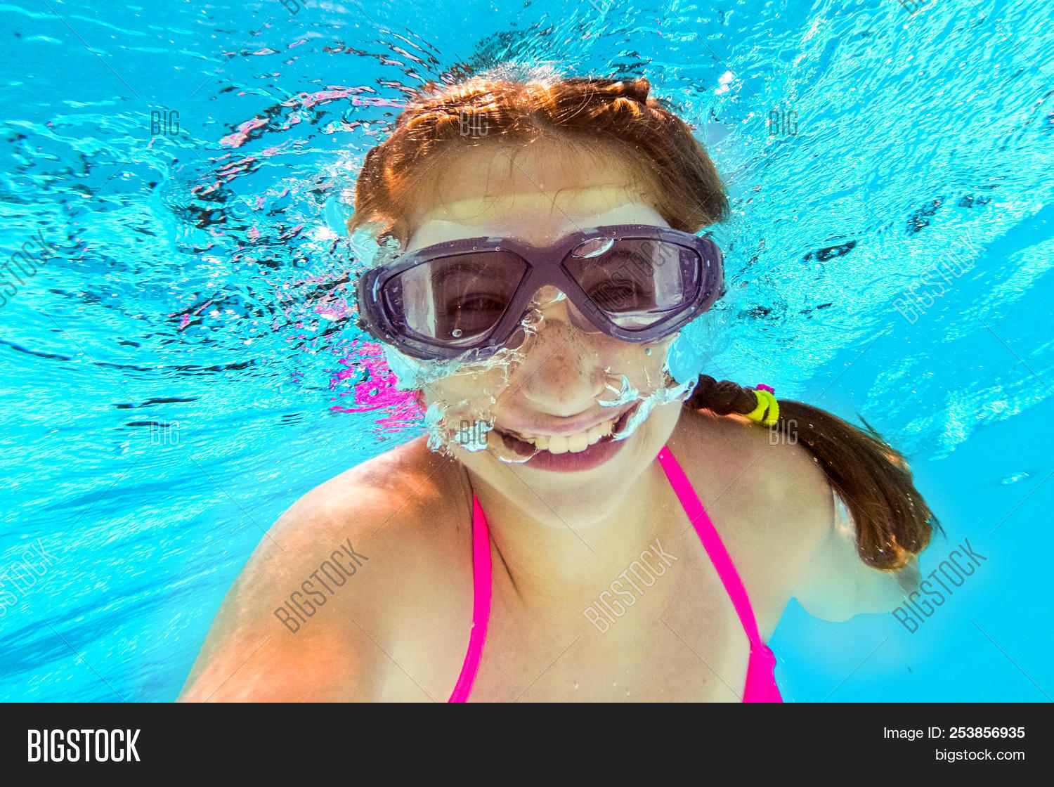 Smiling little girl in swim goggles swimming underwater in pool ...
