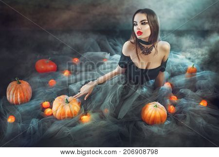 Halloween Witch with Pumpkins and magic lights in a dark room. Beautiful young sexy woman in witches