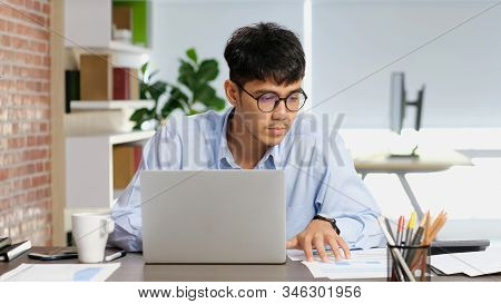 Asian Man At Office, Young Asia Businessman Concentrate On Paper Work While Working With Laptop Comp