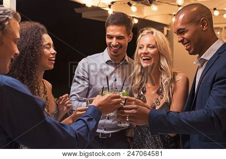 Group of young multiethnic friends enjoying evening and drinking cocktails. Happy men and women rais