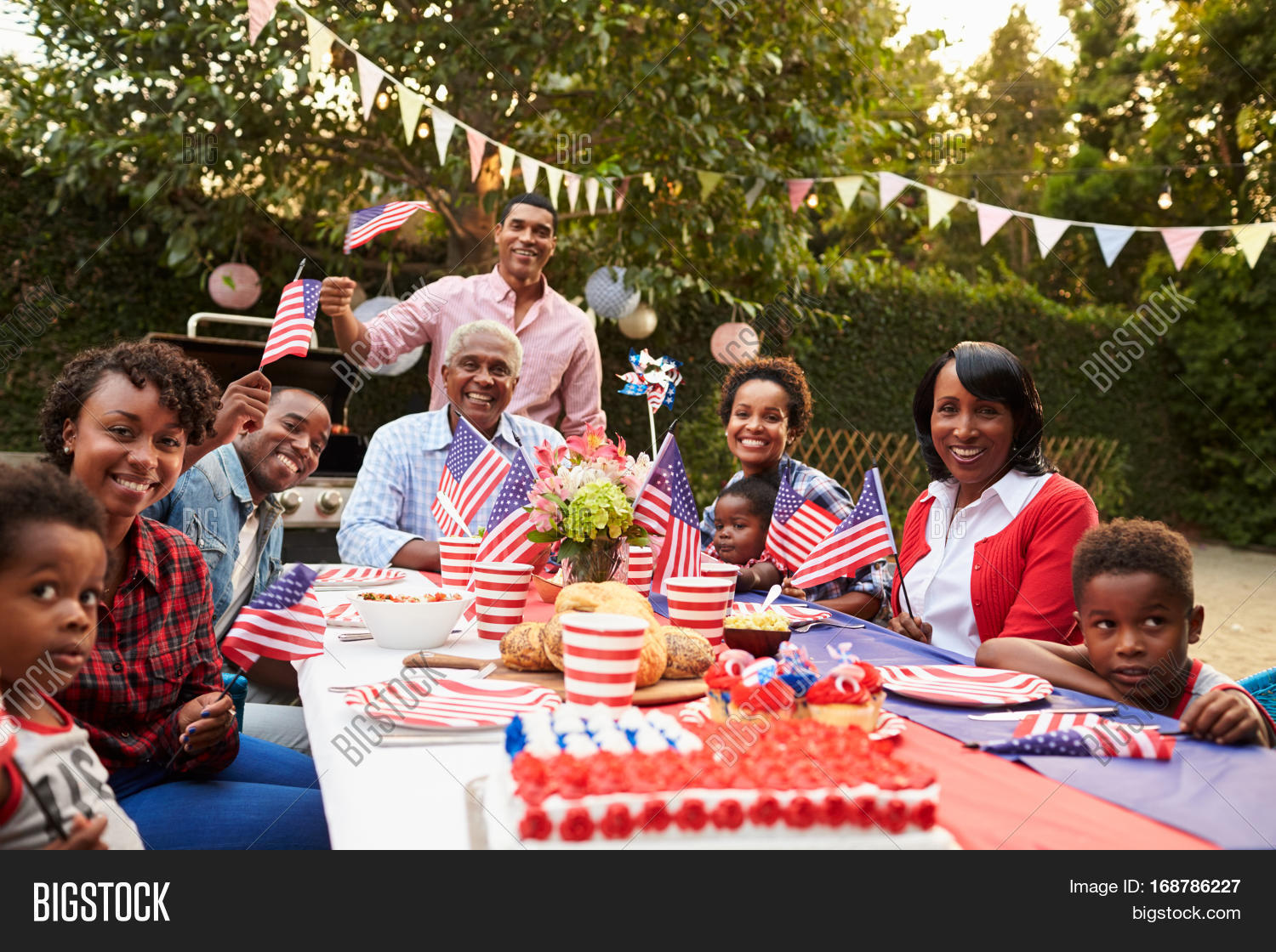 30s,4th july,60s,adults,african american ethnicity,black,boys,brother,celebrating,children,copy space,dad,day,father,filipino ethnicity,food and drink,garden,grandfather,grandmother,grandparents,grandson,holiday,horizontal,in laws,independence day,kids,looking at camera,medium group of people,men,millennials,mixed race person,mother,multi ethnic group,multi generation family,mum,outdoors,parents,party,pre-teens,seniors,siblings,sitting,son,table,toddler,togetherness,tradition,waving flag,women,young adults
