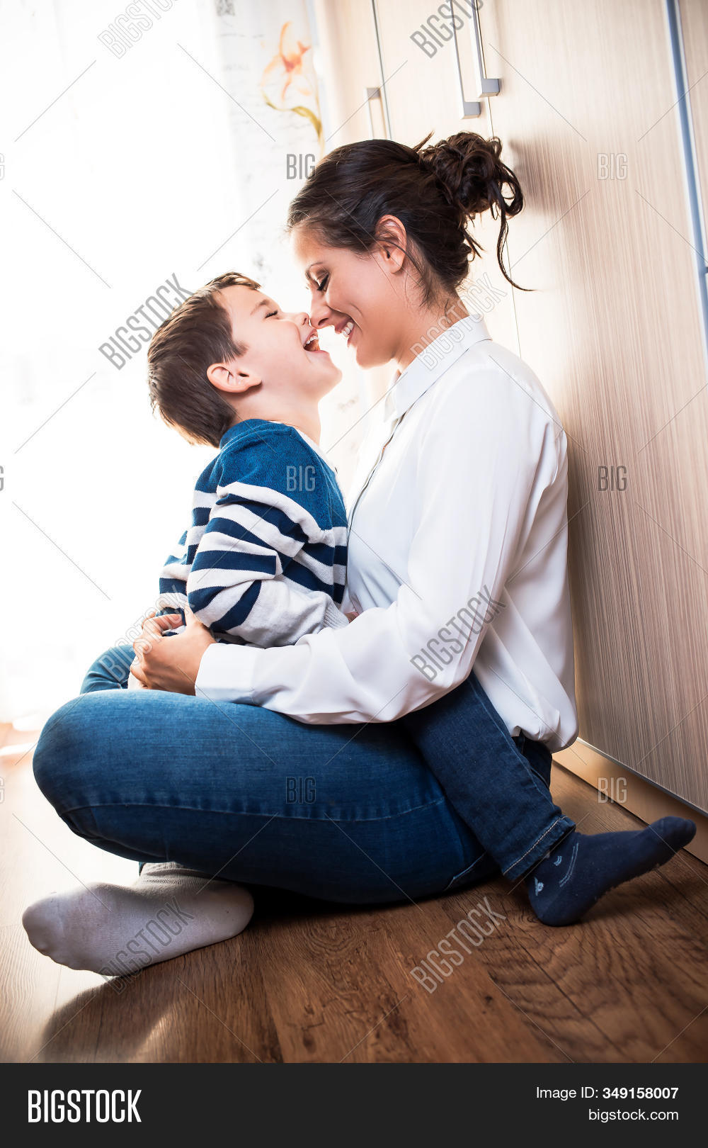 care,smiling,indoors,playing,lap,sitting,tenderness,relationship,adorable,affectionate,affection,hug,kiss,smile,motherhood,parenthood,holding,joyful,parenting,blue,white,cheerful,adult,leisure,home,beautiful,lifestyle,together,cute,portrait,two,fun,little,happy,parent,female,happiness,caucasian,people,young,childhood,boy,mom,woman,child,son,mother,kid,love